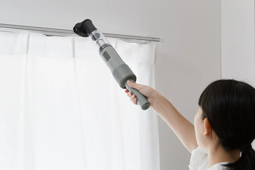 女性がカーテンレールを掃除機で掃除している様子