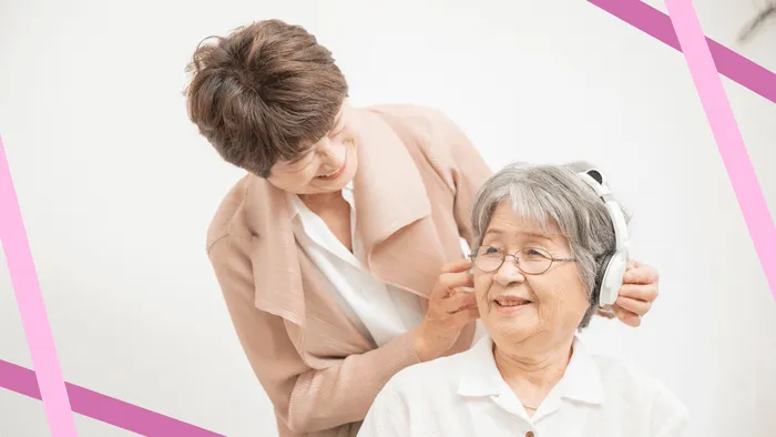 イヤホンを装着する高齢女性とその介護者の様子を描いた画像です。
