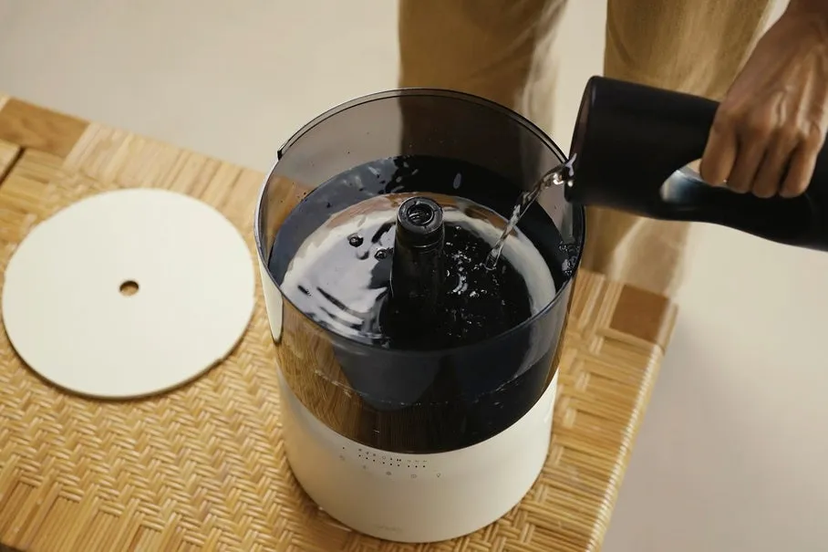 加湿器に水を入れている様子を写した写真。加湿器は白と黒のデザインで、蓋が外されており、水が注がれている。