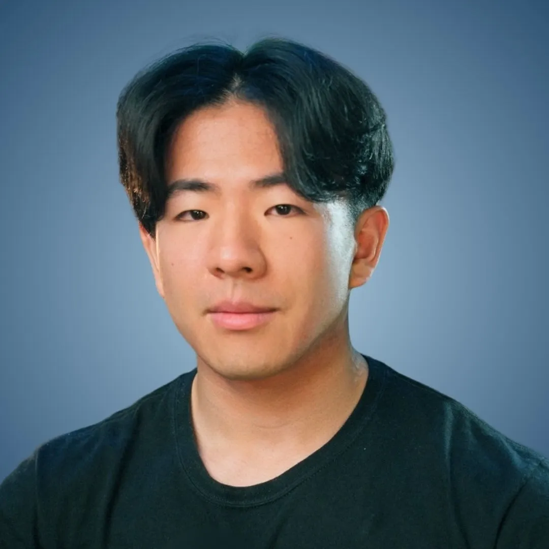 黒いTシャツを着た東アジア系の男性のポートレート。背景は青色。