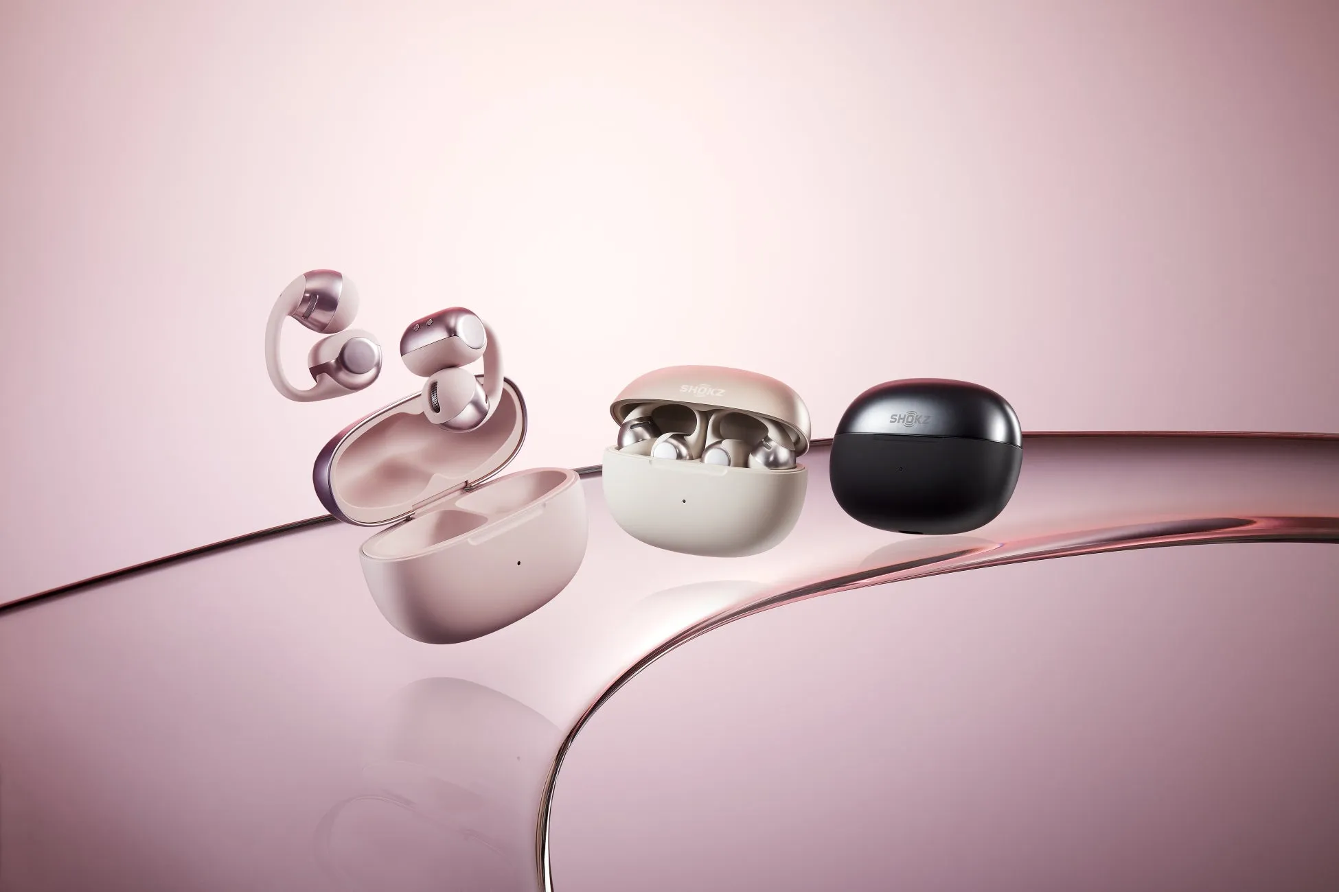 ピンク色の背景に、さまざまなデザインの Shokz のワイヤレスイヤホンが写っています。左には、ケースが開いた状態のイヤホンがいくつかあり、右には、ケースが閉じているイヤホンがいくつかあります。