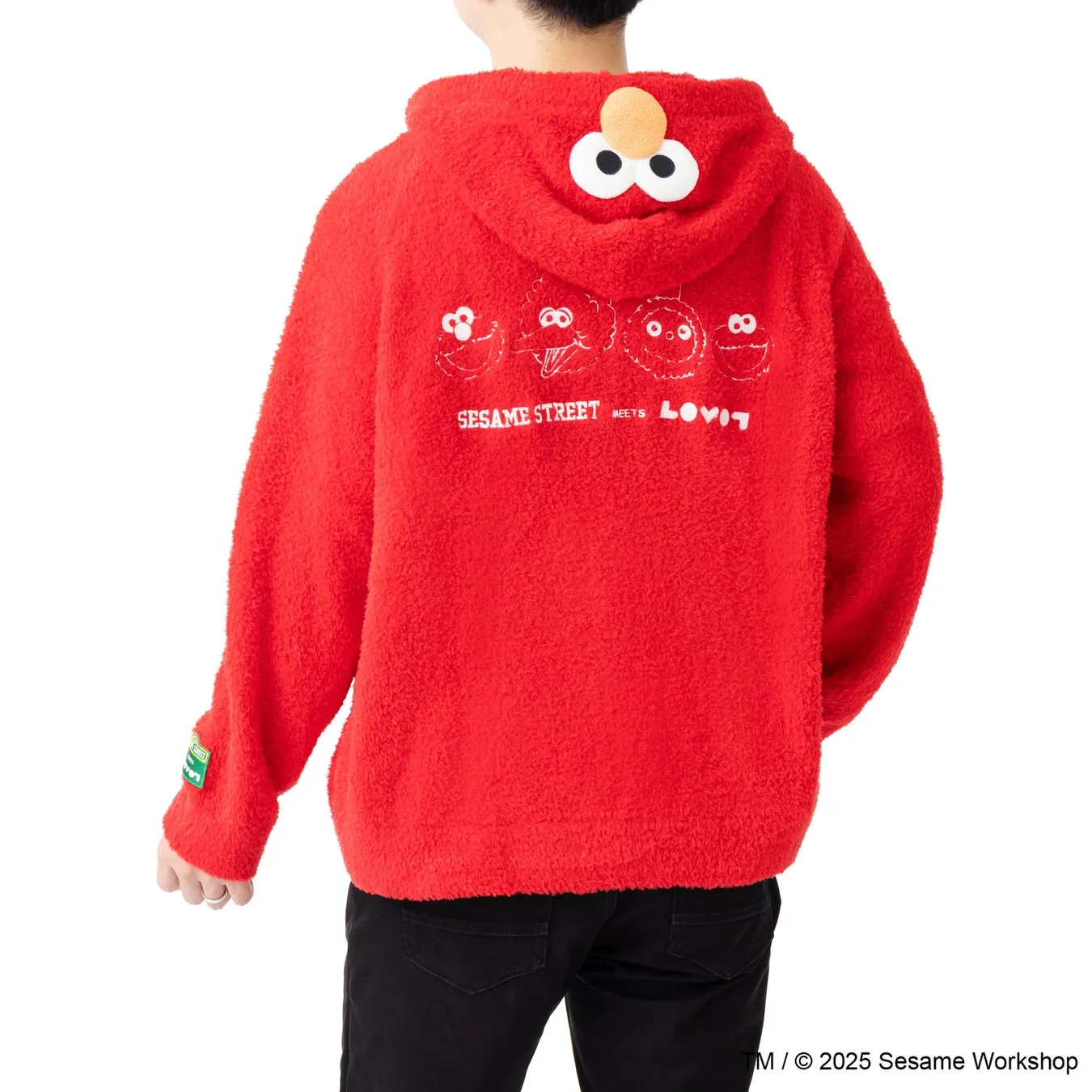 セサミストリートのエルモがデザインされた赤いパーカーを着た人物の後ろ姿を捉えた写真です。パーカーのフードにはエルモの顔が施され、背中にはセサミストリートのキャラクターとロゴが描かれています。