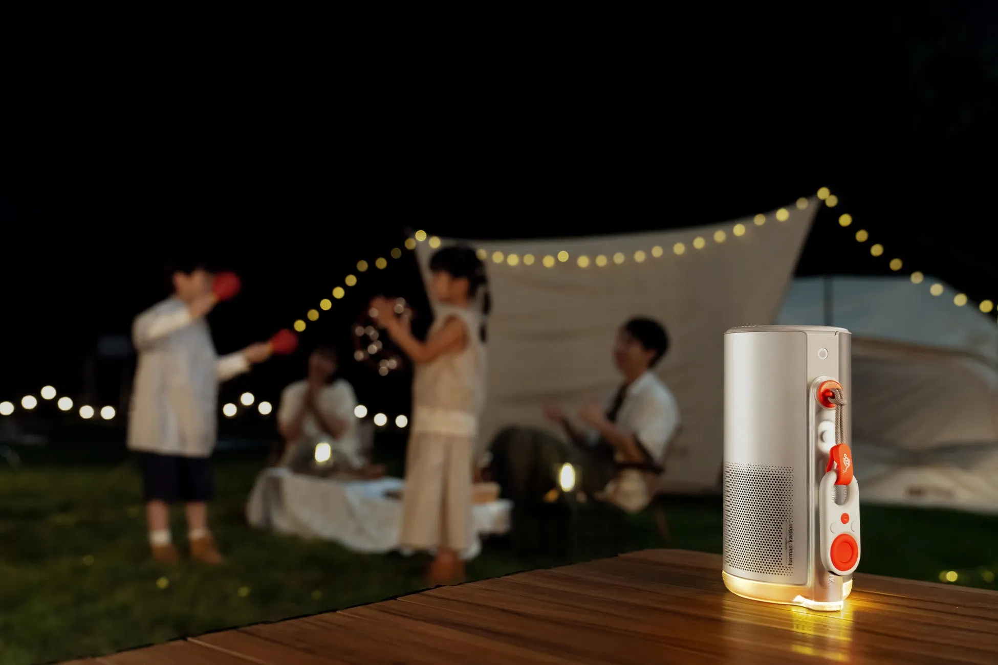 夜のキャンプ場で音楽を聴きながら楽しむ家族の様子。手前にはスピーカーが置かれ、子供たちが楽しそうに遊んでいる。