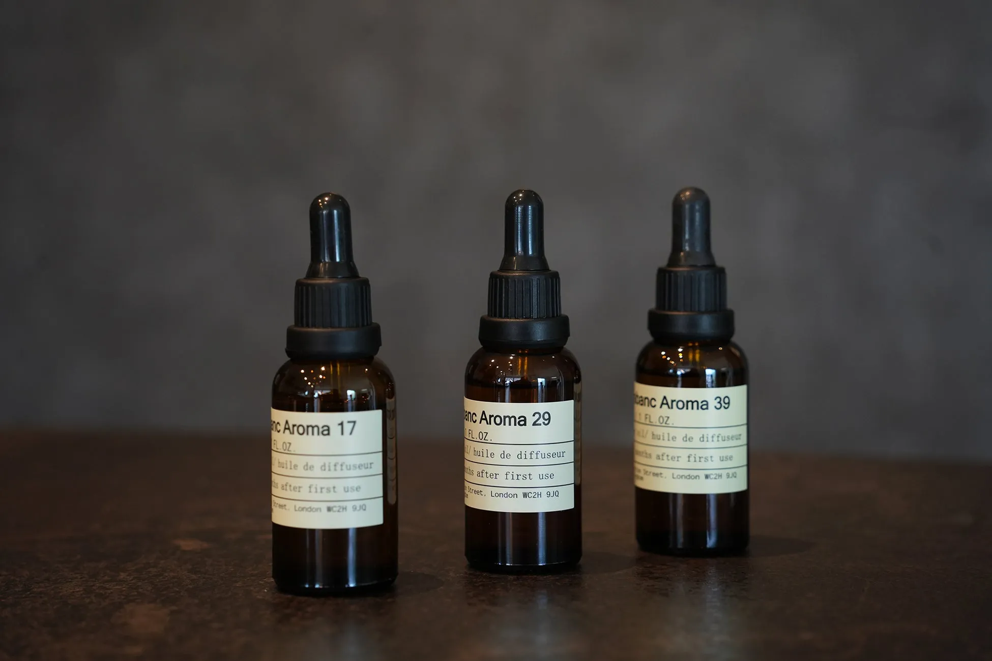 3つのボトルが並んで配置された写真。各ボトルには白いラベルが付いており、テキストが記載されている。背景は暗い色で、ボトルが配置されている表面も暗い色である。