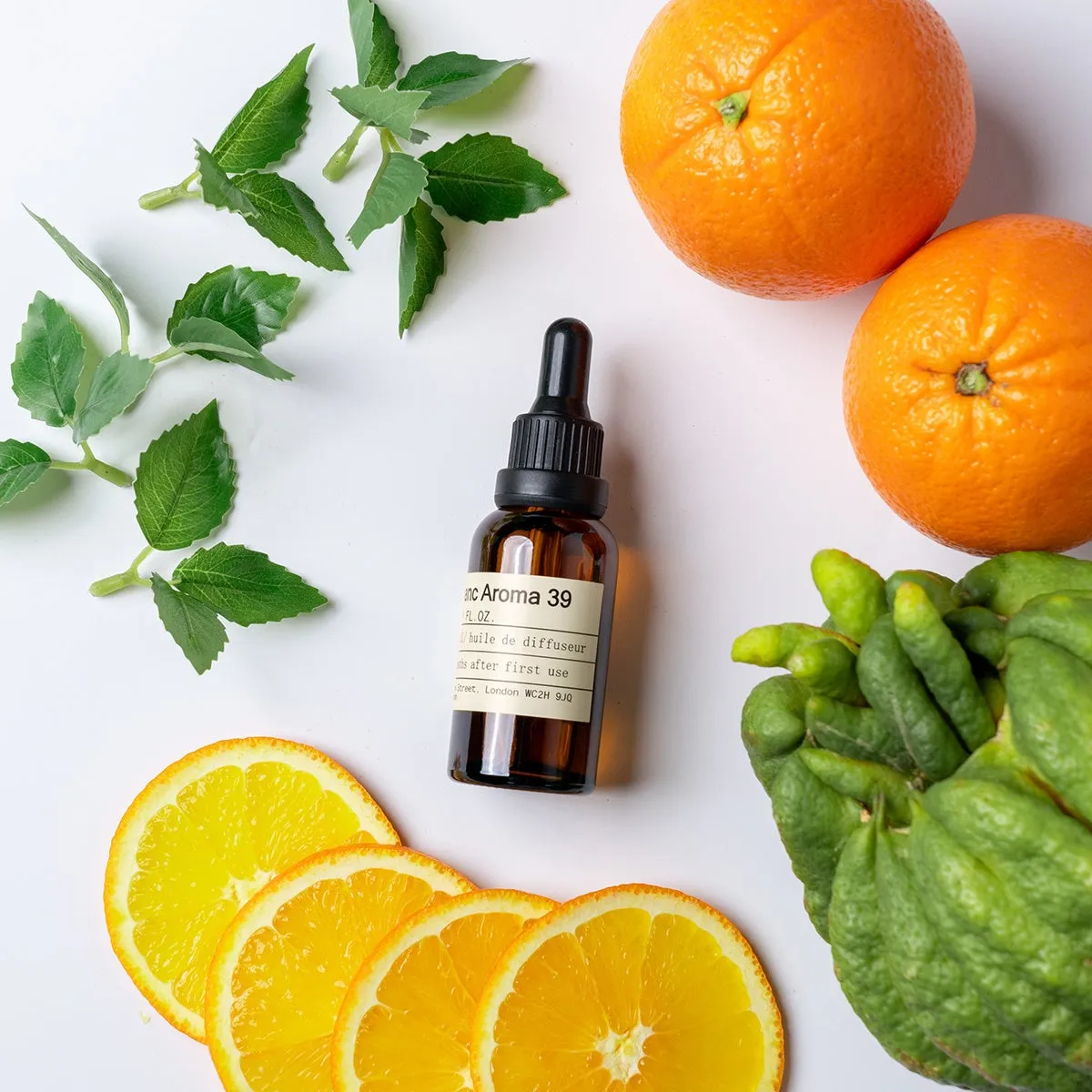 オレンジと葉っぱ、アロマオイルのボトルが置かれた写真です。オレンジは半分にカットされたものと丸ごとのものがあり、葉っぱは緑色です。アロマオイルのボトルにはラベルが付いています。