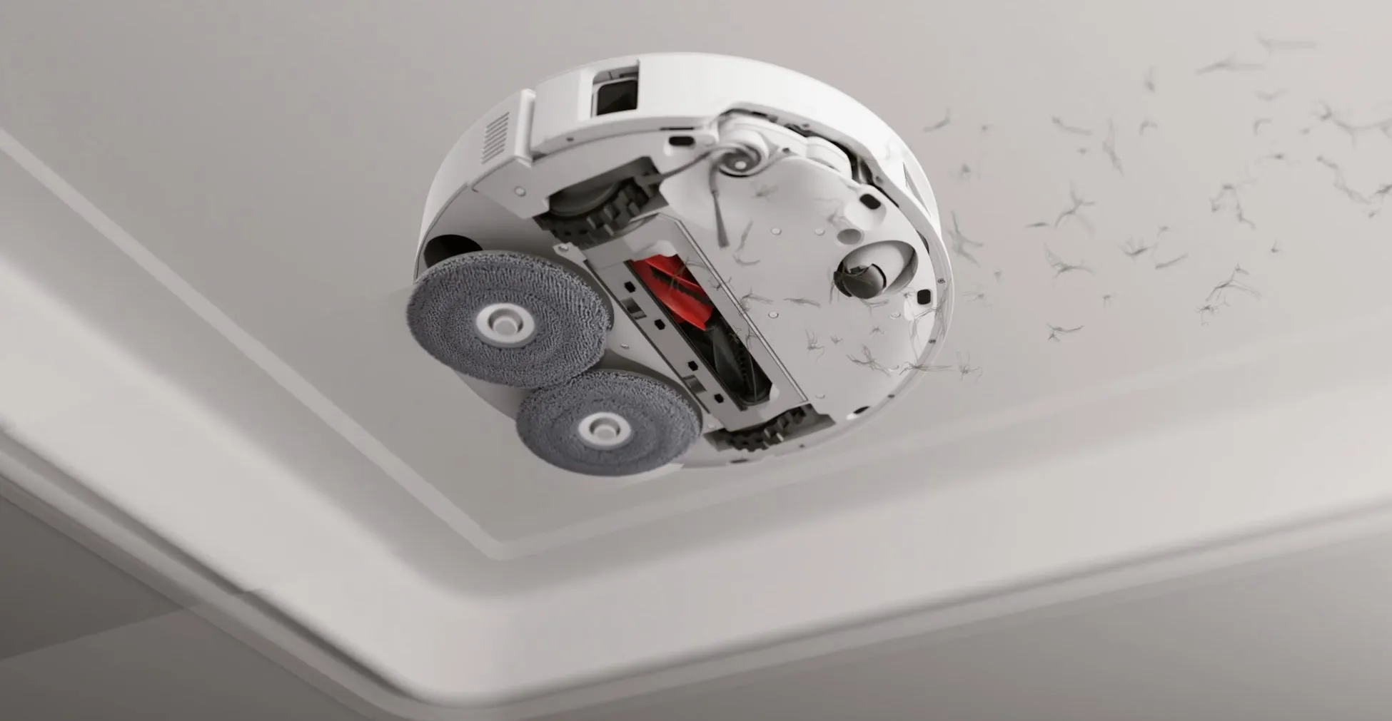 天井を掃除しているロボット掃除機の写真。掃除機は白く、2つの円形の清掃パッドと赤色のブラシが付いている。掃除機は天井に付着したほこりを掃除しているように見える。