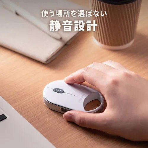 木製のテーブルの上に置かれた白いマウス。マウスに手を置いている様子が写っています。マウスの隣には、紙とコーヒーカップが置かれています。