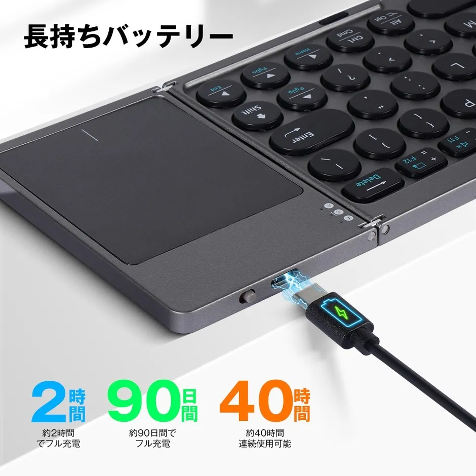 ワイヤレスキーボードの充電中の写真。キーボードはグレーで、右側に丸いキーがあり、左側にはタッチパッドがあります。充電時間は約2時間で、90日間フル充電でき、40時間連続使用可能です。