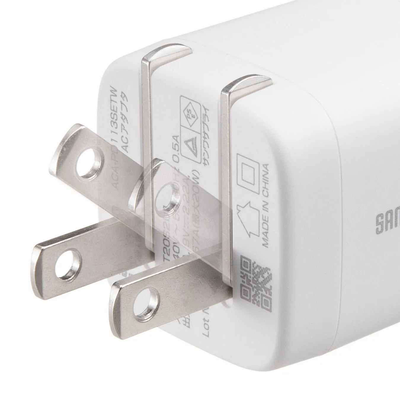 白いACアダプターのクローズアップ画像。プラグが手前にあり、アダプター本体には文字が印刷されている。