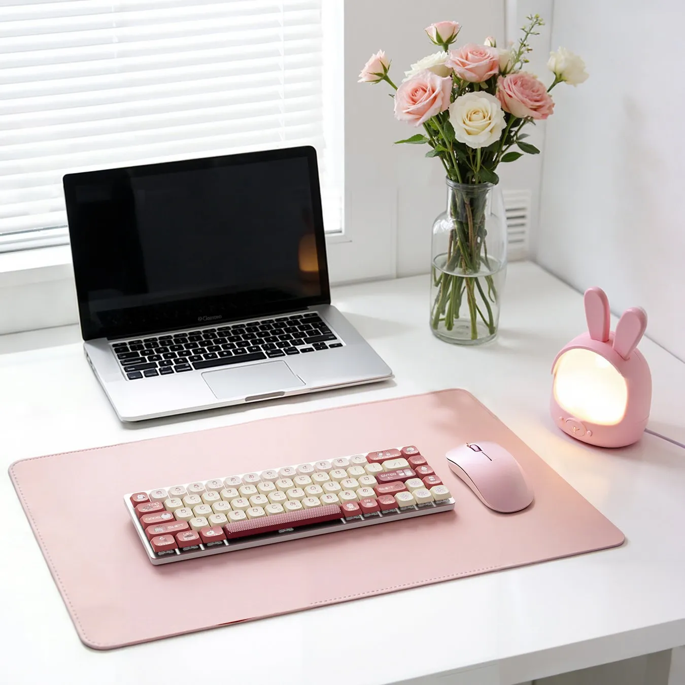 ピンク色のデスク周りの写真。ノートパソコン、キーボード、マウス、ウサギの形をしたランプ、花瓶に入った花が写っている。