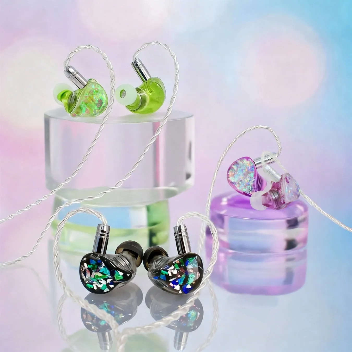 透明な台座に置かれた、さまざまな色のインイヤーイヤホンのクローズアップ写真。イヤホンは、緑、紫、黒のさまざまな色合いで表示されます。