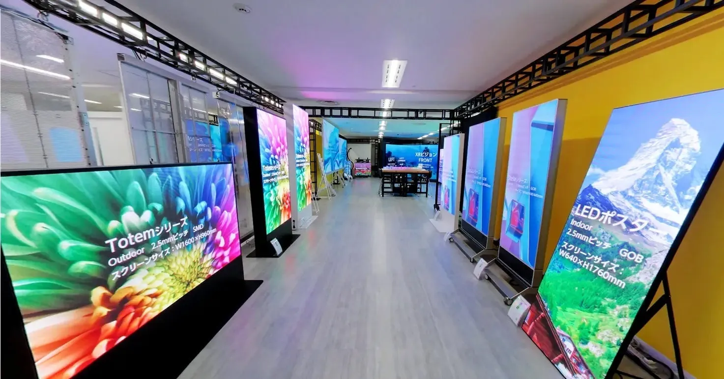 LEDディスプレイが並んだ展示会のような画像です。通路の両側に様々なサイズのLEDディスプレイが配置されており、それぞれ異なる映像を表示しています。奥には、XRビジョンと書かれた看板が見えます。